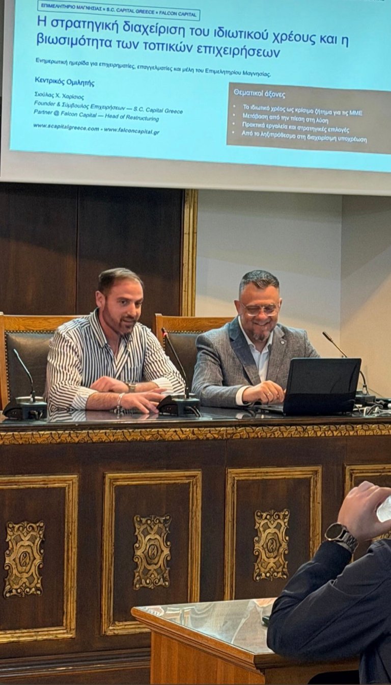 Δύο άνδρες σε πάνελ ημερίδας με slide προβολής στο Επιμελητήριο Μαγνησίας